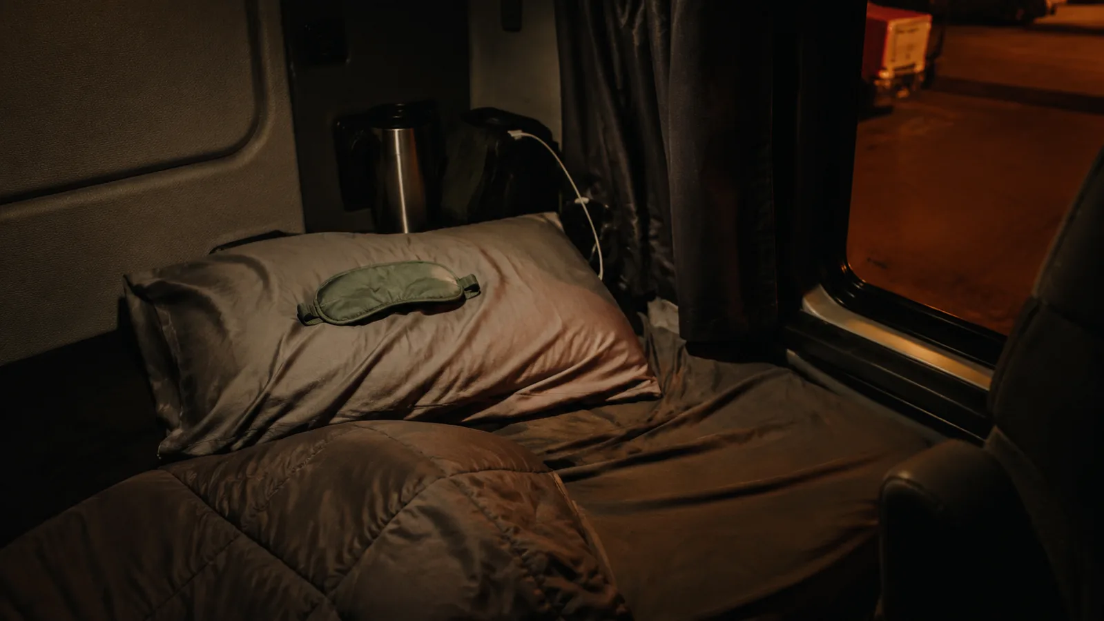 A sage green weighted sleep mask resting on a folded blanket inside a dim truck sleeper cab at night