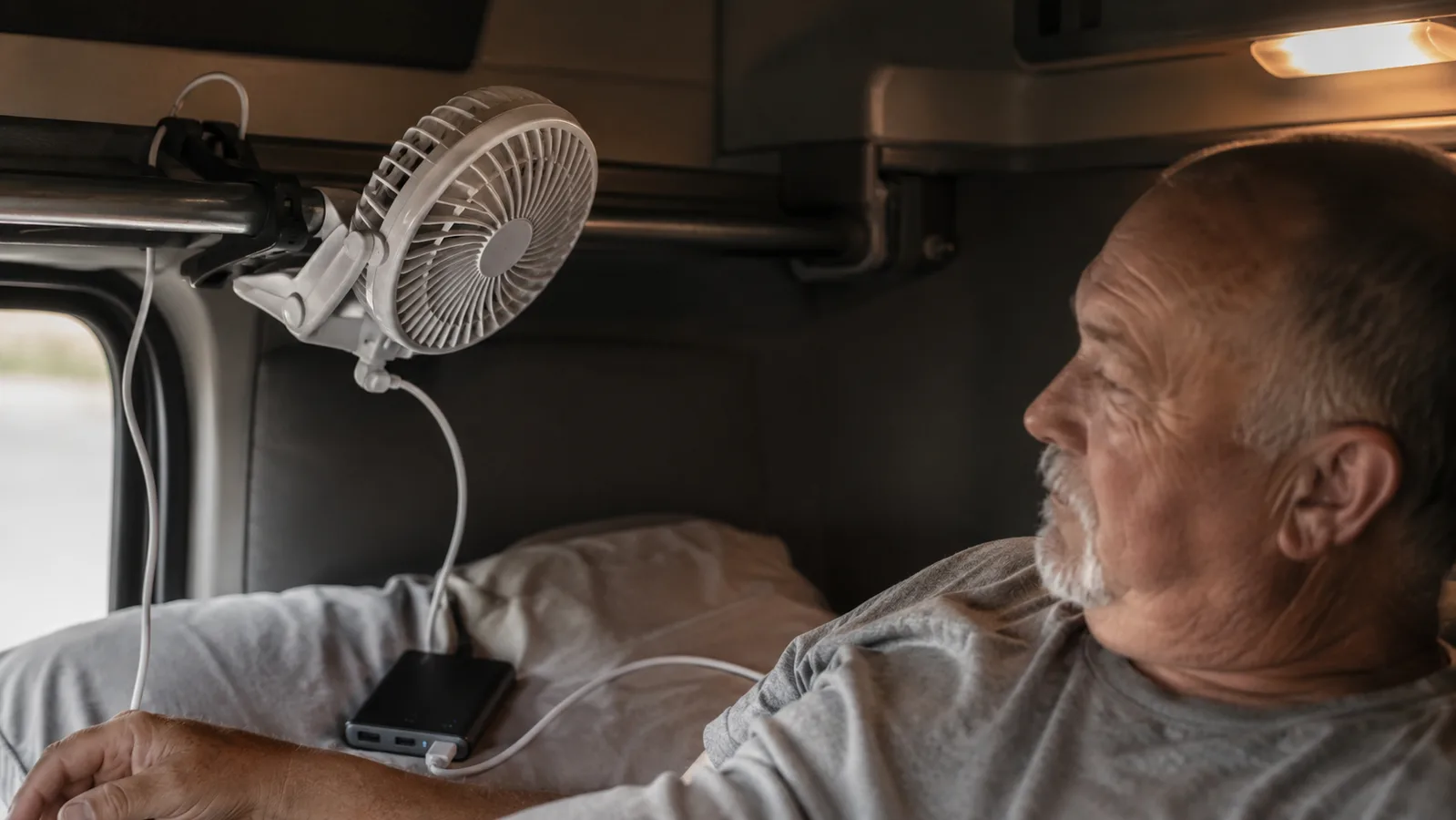 A BESKAR clip fan clamped to a metal bunk rail inside a truck sleeper cab, angled toward the pillow